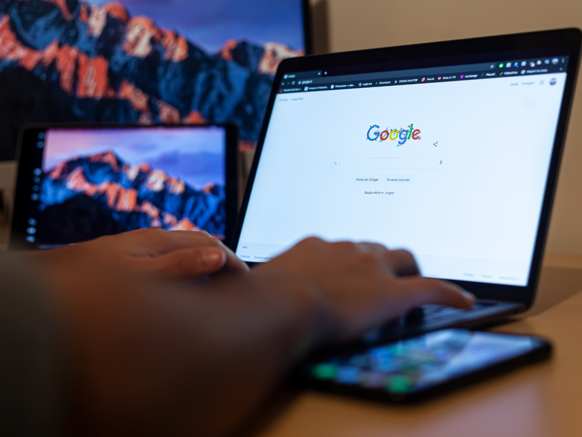 A person is typing on a laptop computer with a google search bar on the screen.