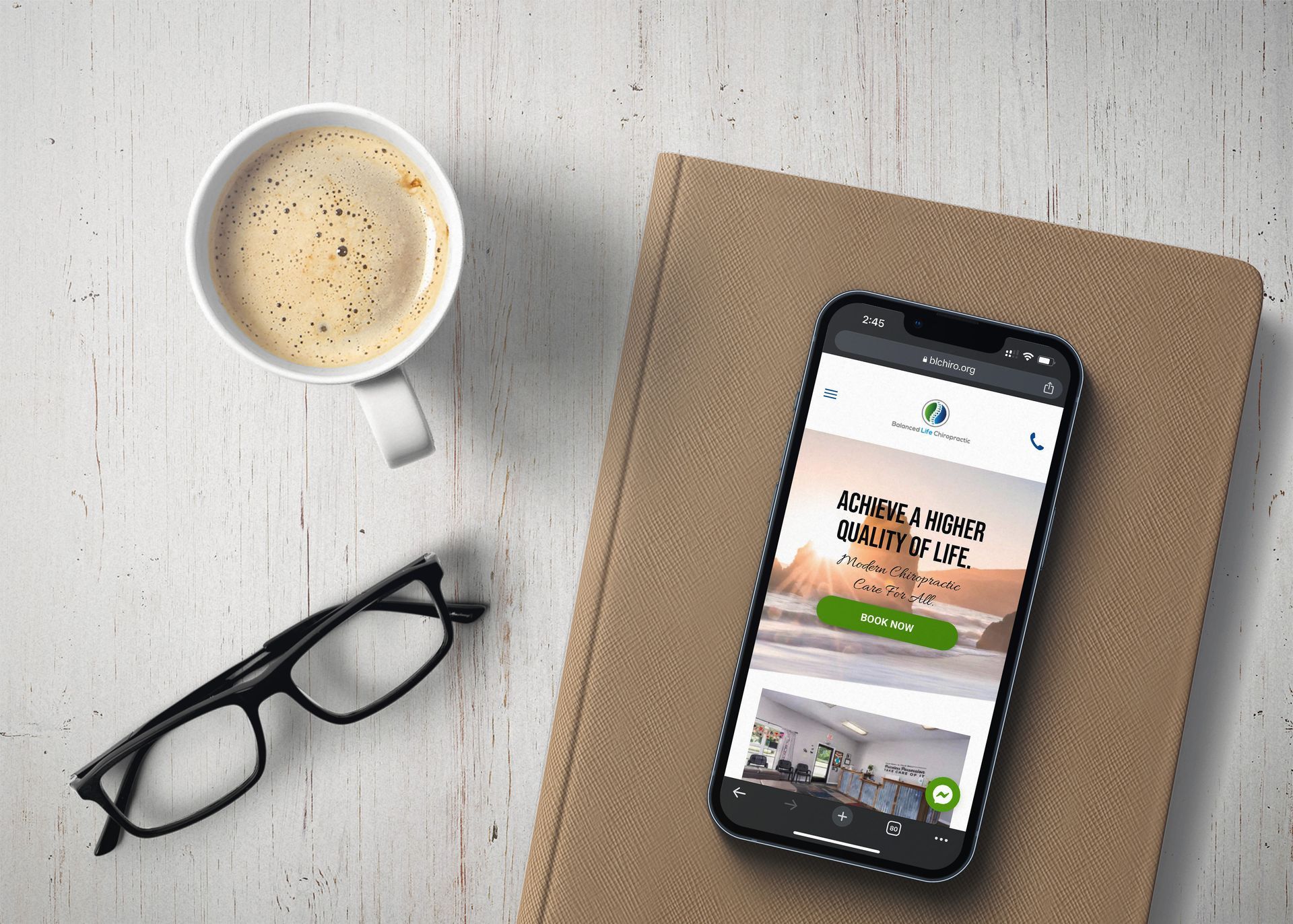 A cell phone is sitting on top of a book next to a cup of coffee and glasses.