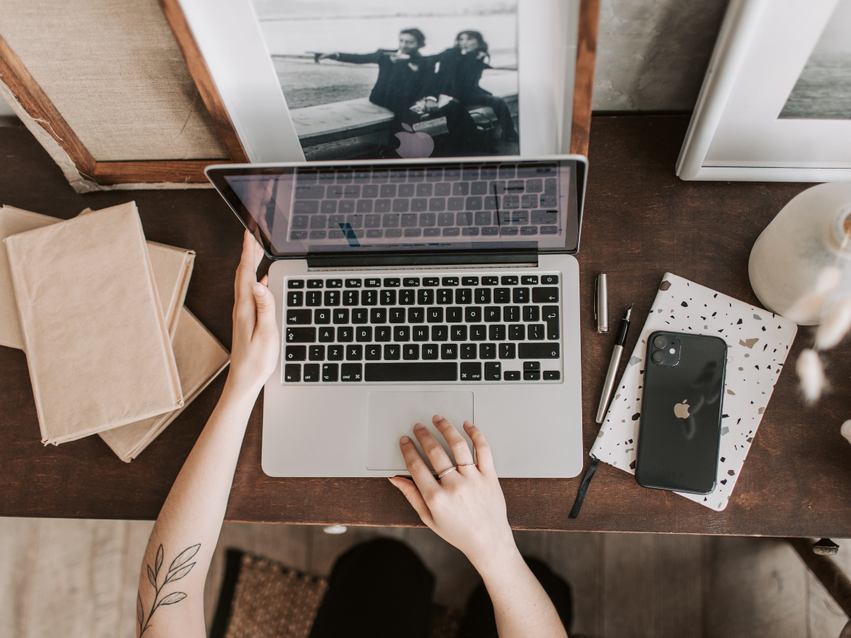 Person using laptop at desk with framed photo and phone.