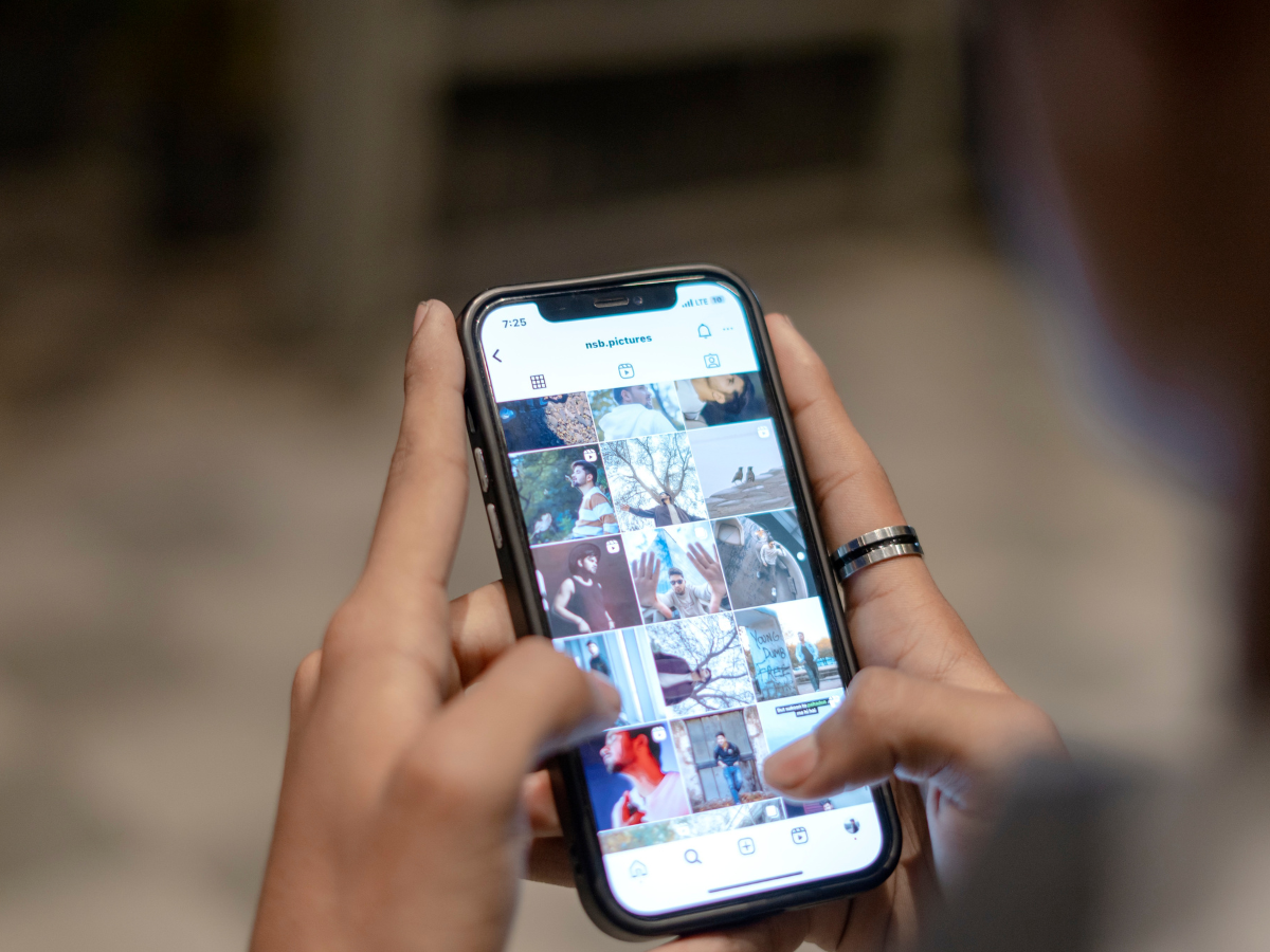 Person holding a smartphone, scrolling through a social media feed with photos; hands visible. Person holding a smartphone, scrolling through a social media feed with photos; hands visible.