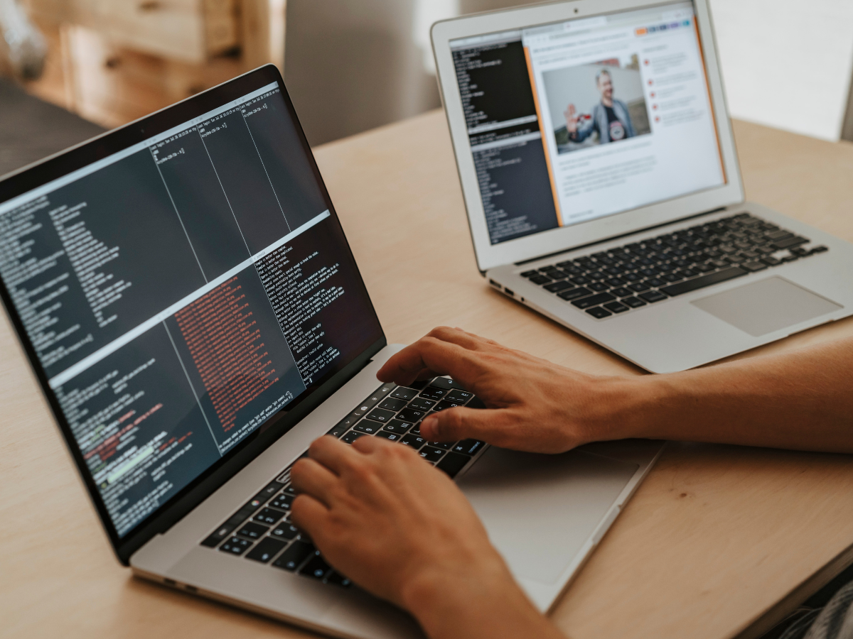 Person coding on a laptop; another laptop open with a webpage. Person coding on a laptop; another laptop open with a webpage.