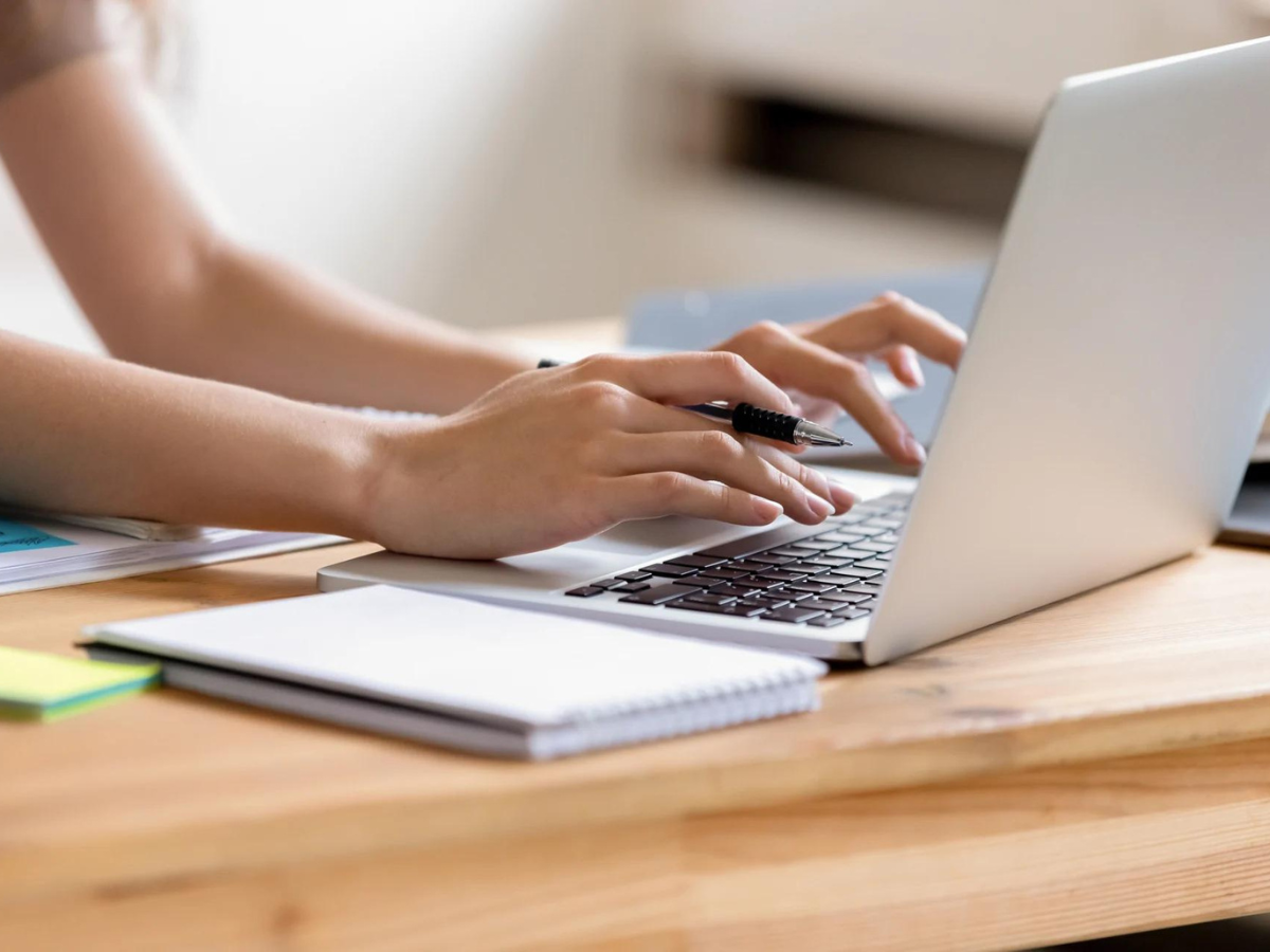 A person is typing on a laptop computer on a wooden table.