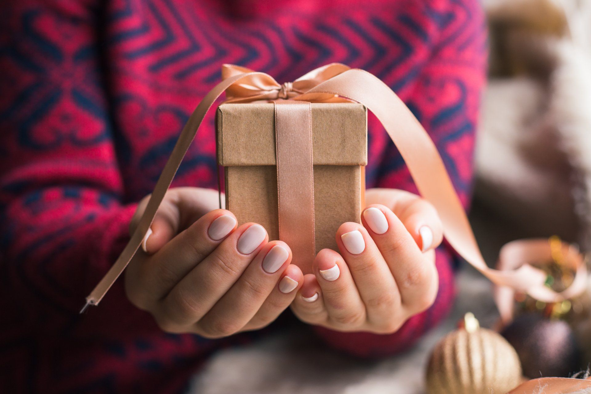 A woman is holding a small gift box with a ribbon in her hands.