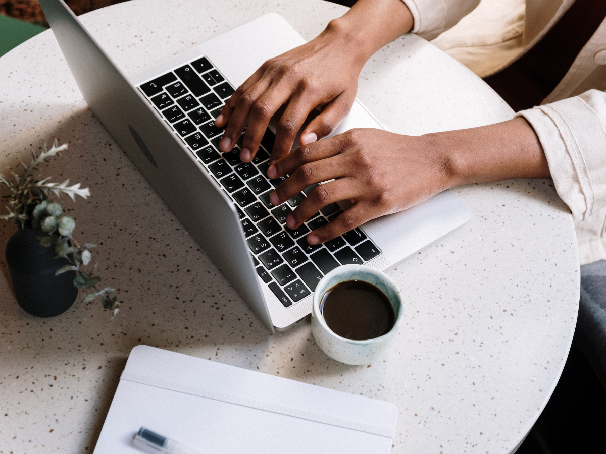 A person is typing on a laptop next to a cup of coffee.