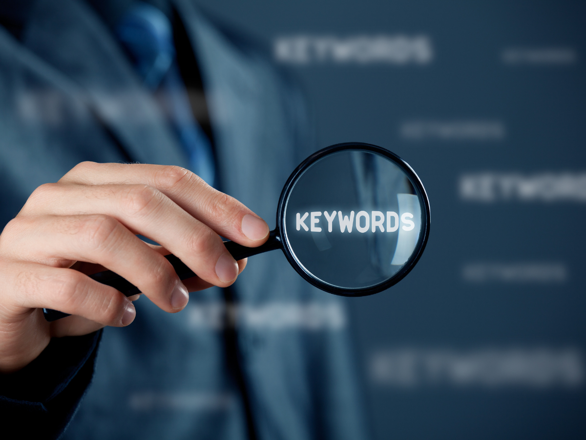 A person is holding a magnifying glass with the word keywords on it