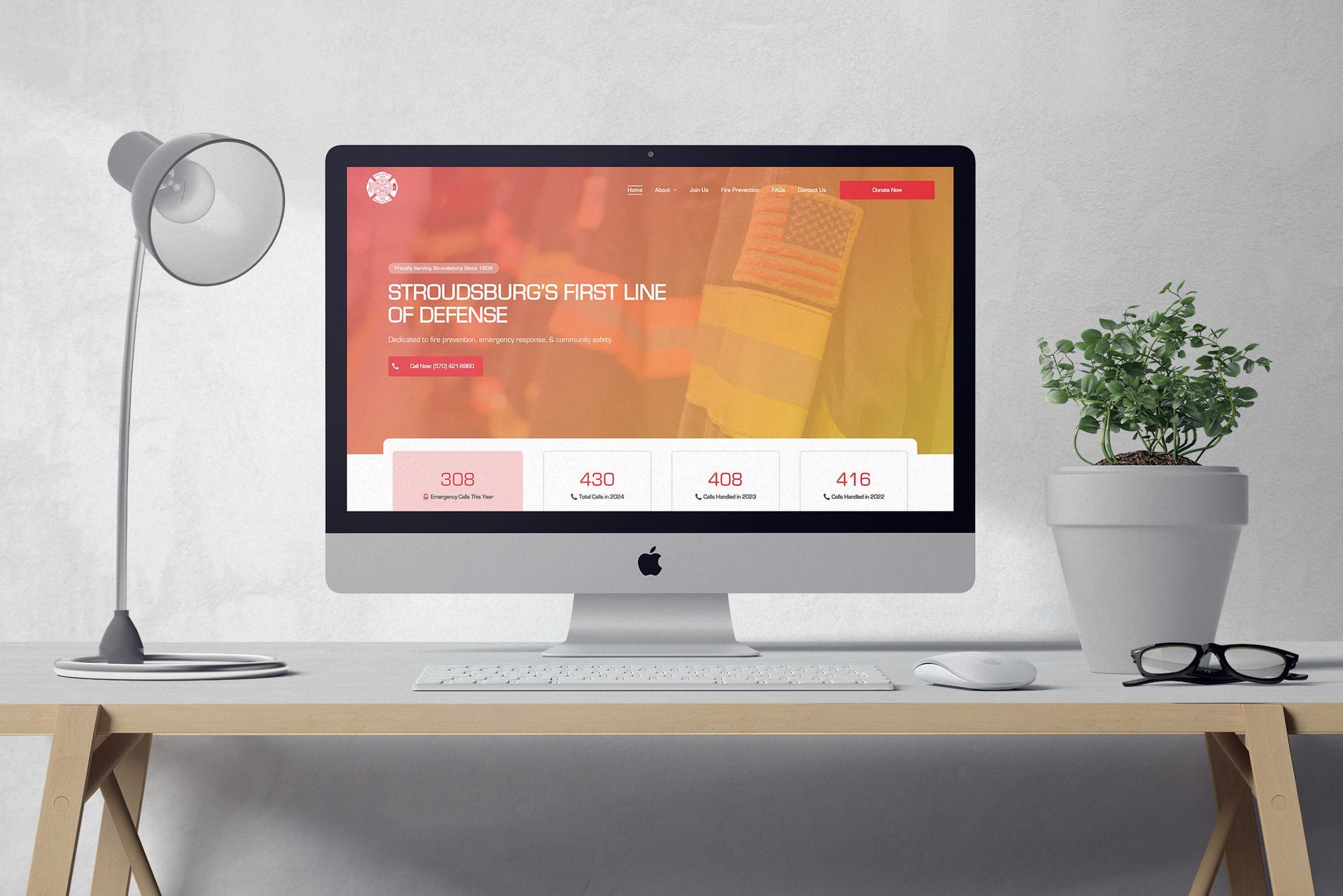 Desktop computer on a desk with a website displaying on the screen, a lamp, and a potted plant.