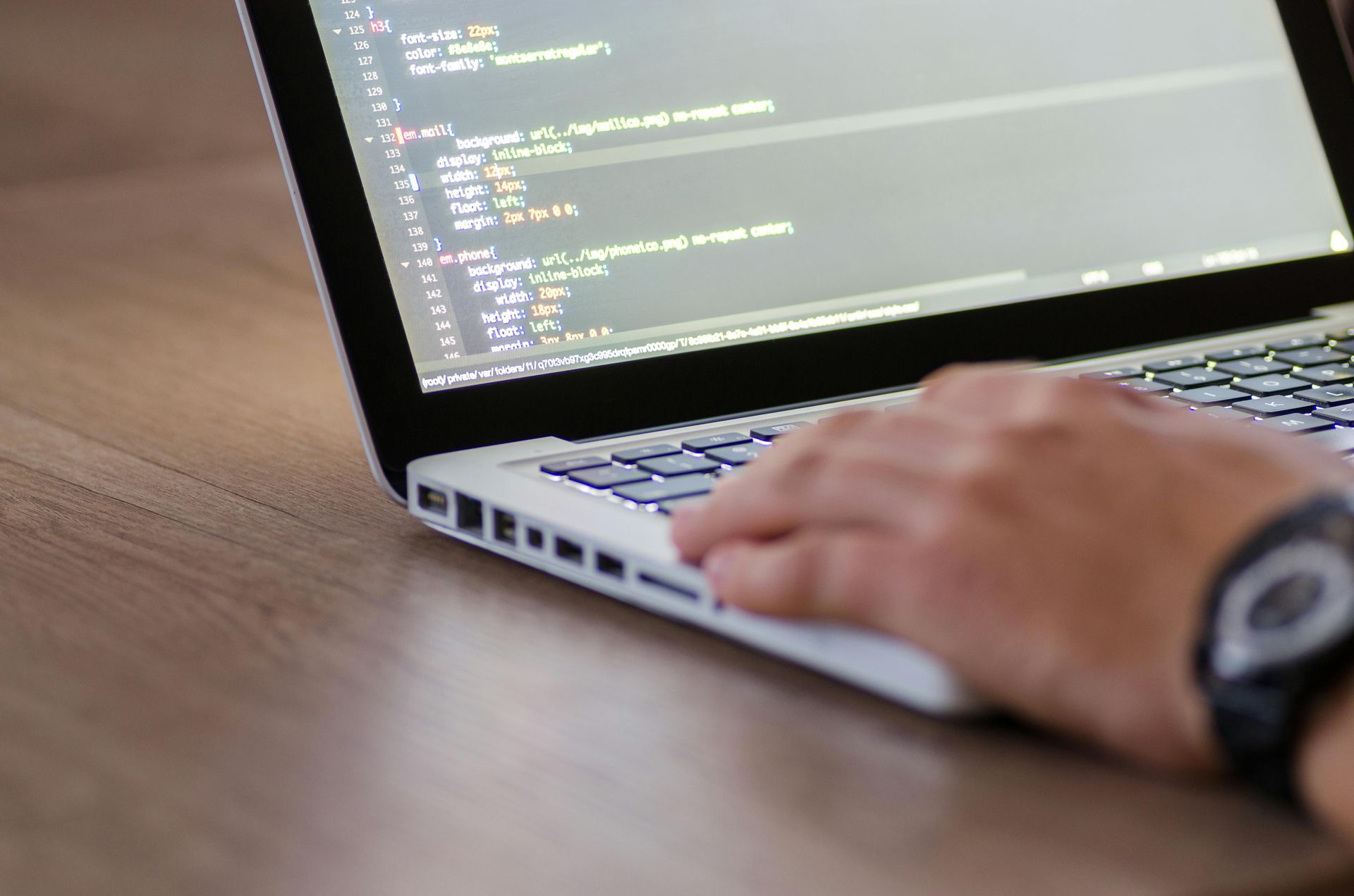 A person is typing on a laptop computer with a watch on their wrist.