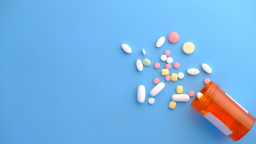 Orange pill bottle tipped over, spilling assorted colorful tablets on a blue background