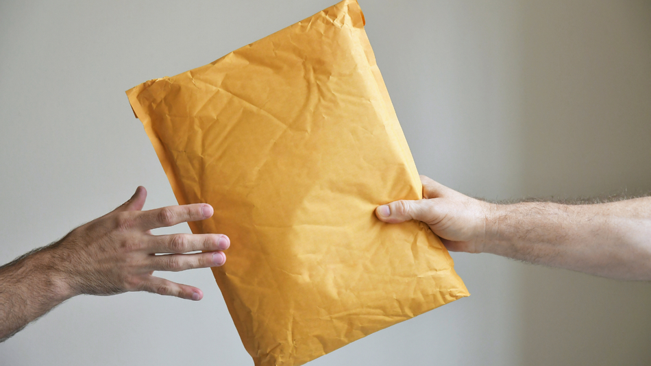 Two hands exchanging a large yellow padded envelope on a plain background