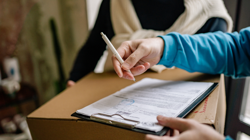 Hands writing on papers atop a clipboard at a table