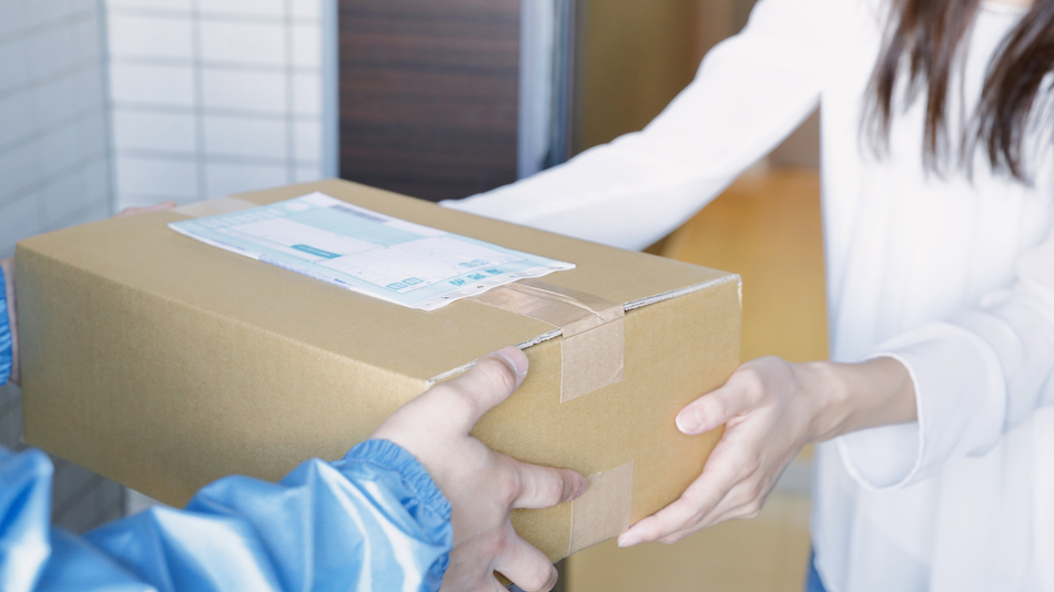 Person handing a cardboard box to another person in a bright indoor setting
