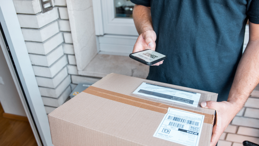 Person holding a handheld scanner over a cardboard package at a doorstep