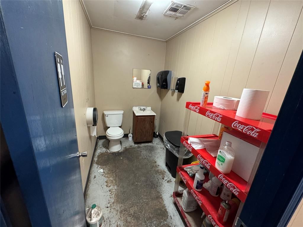 A bathroom with a toilet, sink, and coca cola shelves.