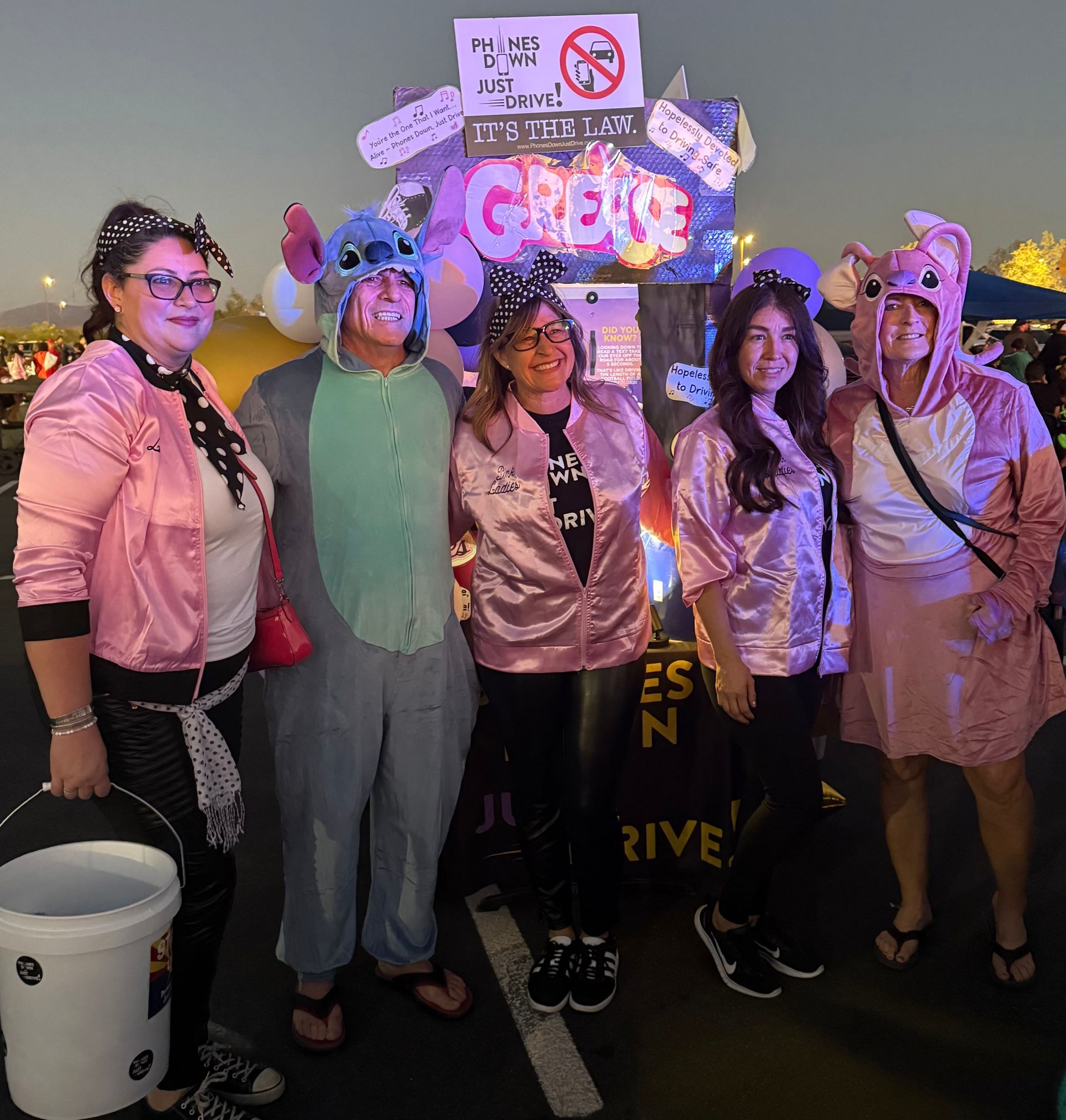 Five people in costumes, including a pink jacket group and a Stitch, posing by a