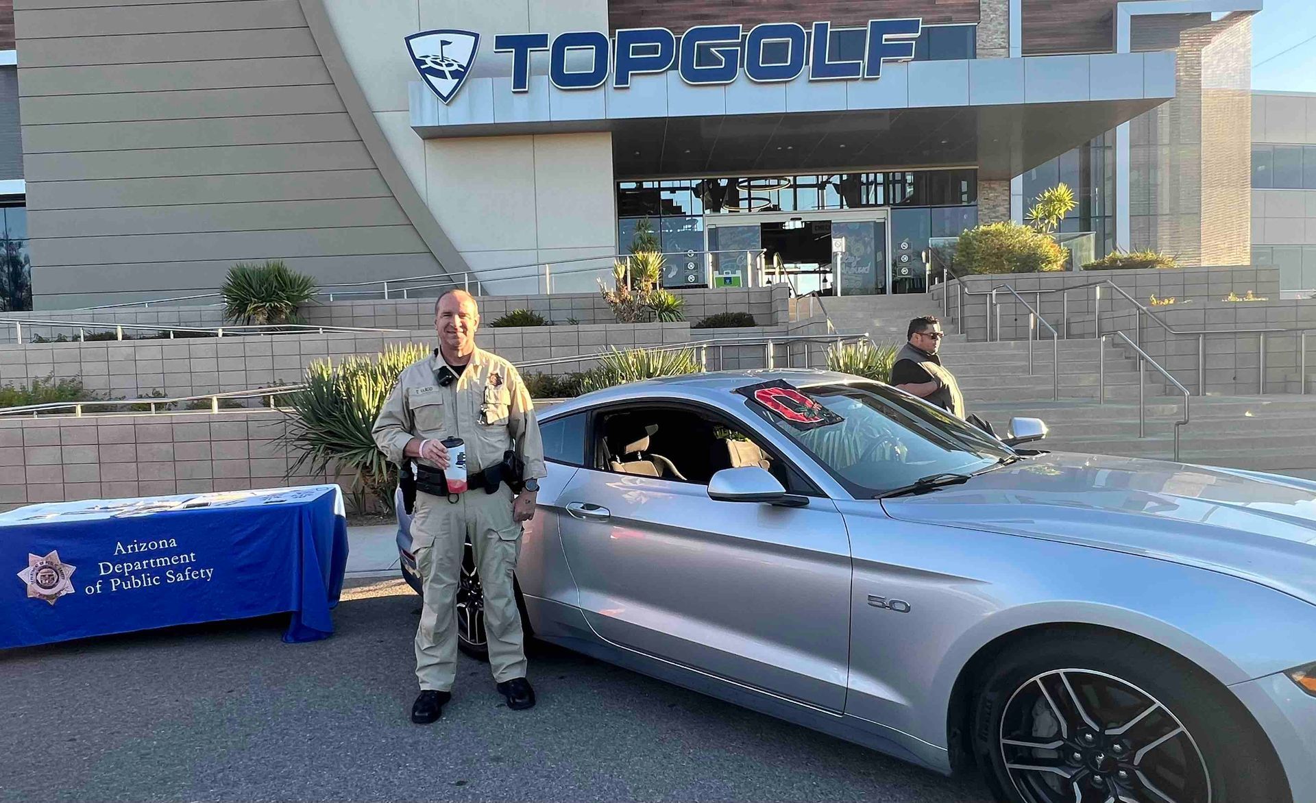 A man is standing next to a silver car in front of a building.
