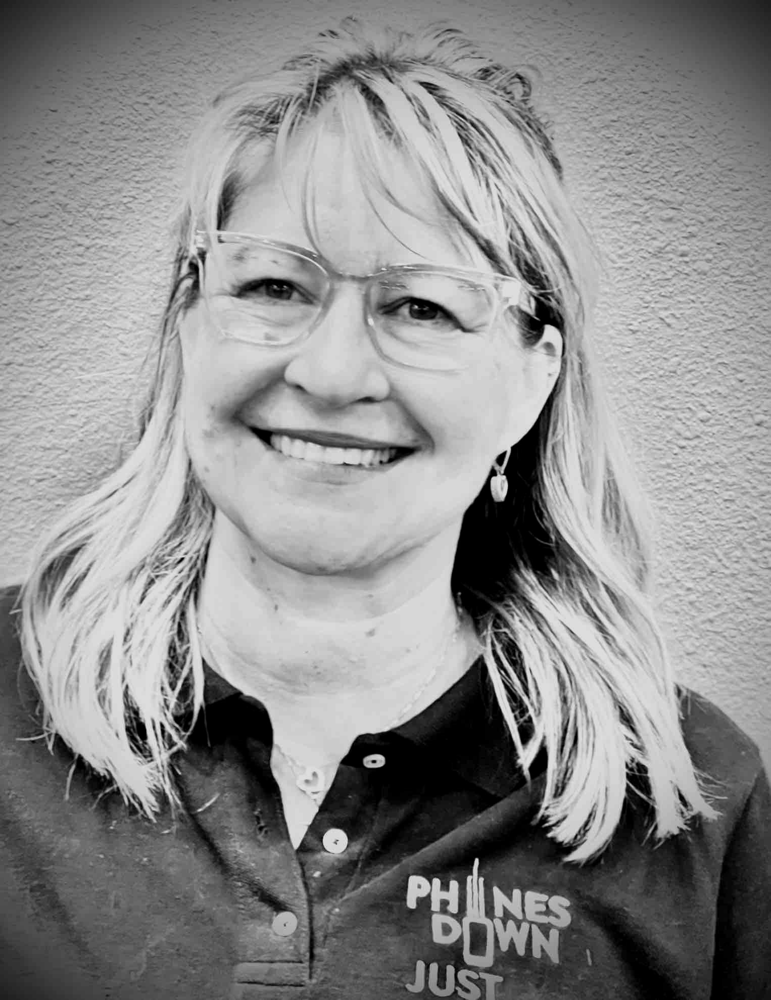A woman wearing glasses and a black shirt is smiling in a black and white photo.