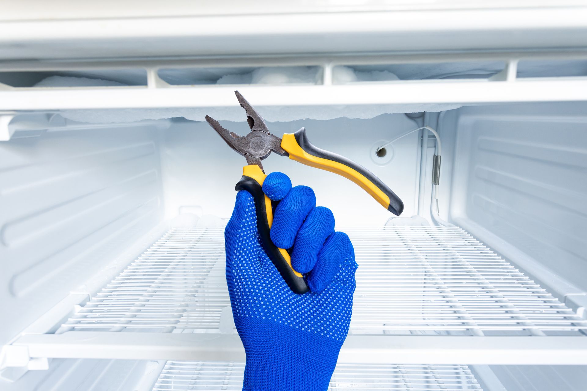 A person is holding a pair of pliers in front of an empty refrigerator.