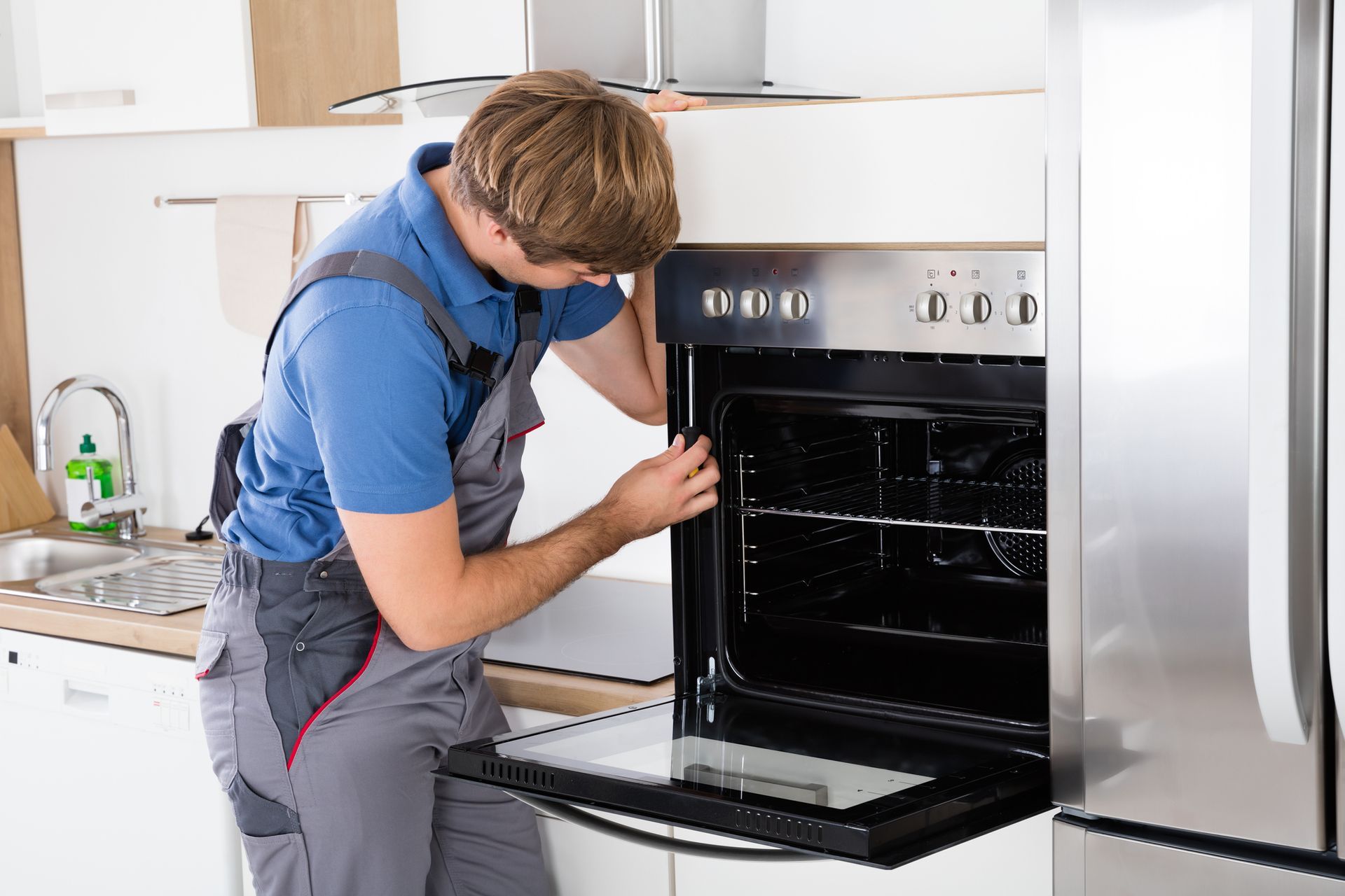 A man is fixing an oven in a kitchen.