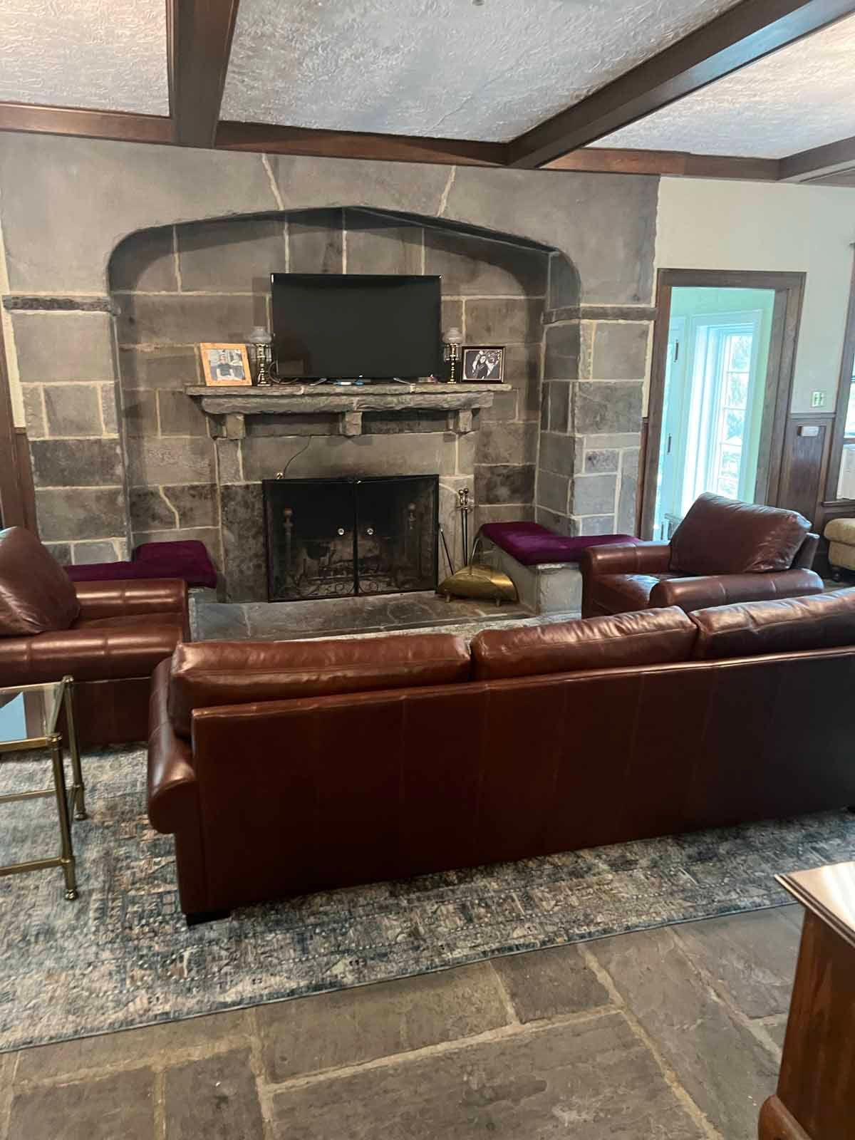 Living room with a stone fireplace, brown leather furniture, and a rug.