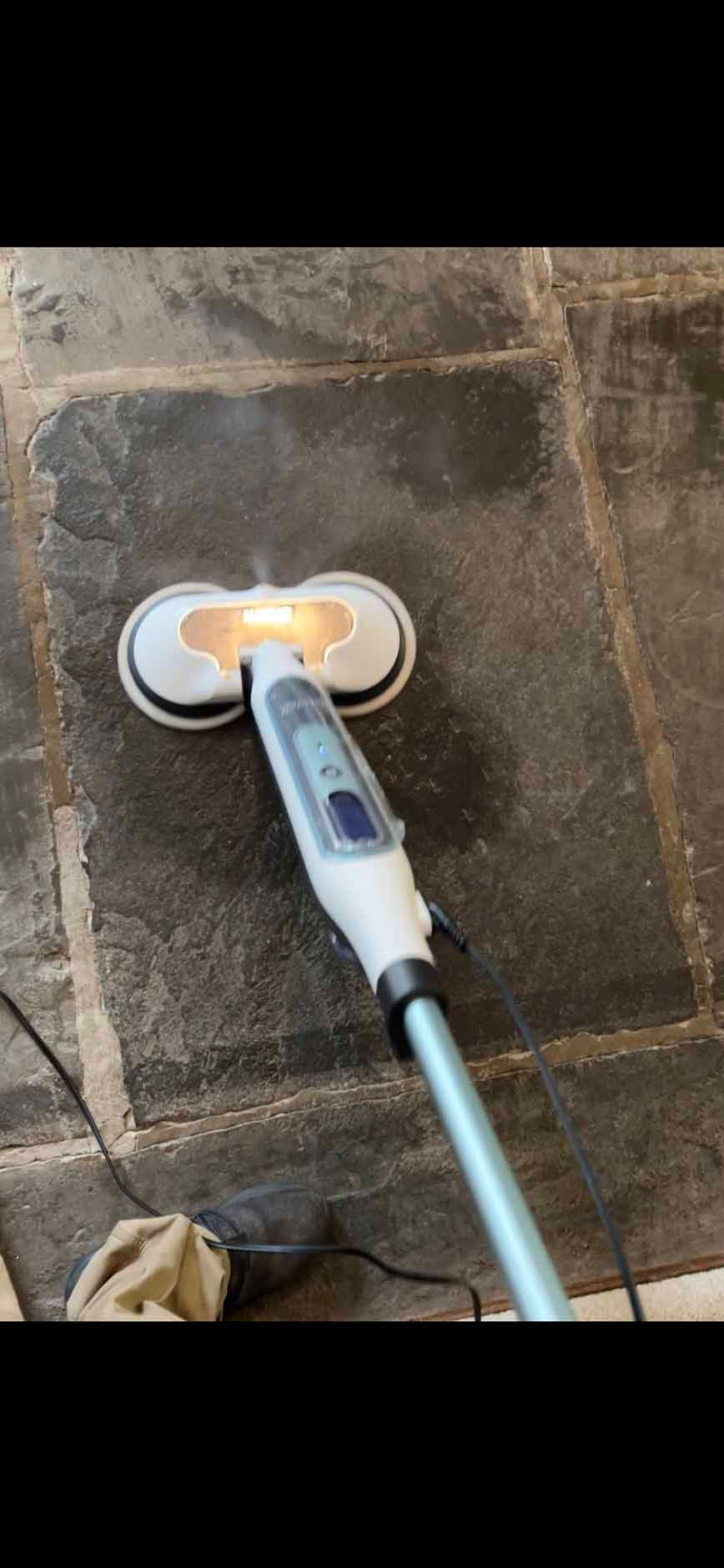 A steam mop cleaning a dark tiled floor, emitting steam.