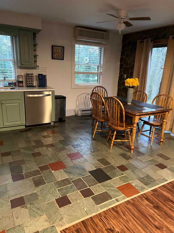 Kitchen with colorful square tile flooring, light green cabinets, stainless steel appliances, and a wooden dining table.
