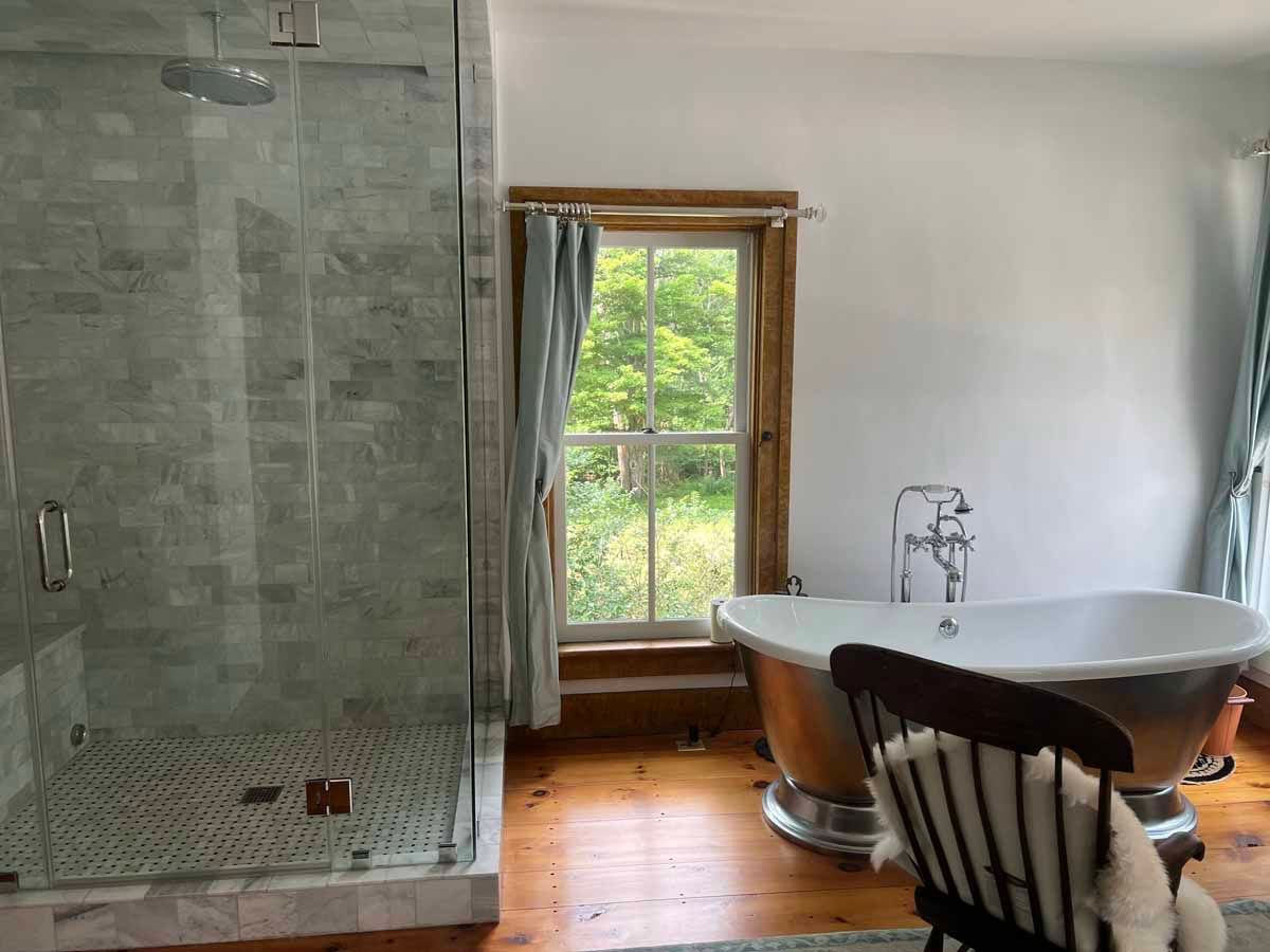 Bathroom with glass shower, clawfoot tub, window, and wood floor.