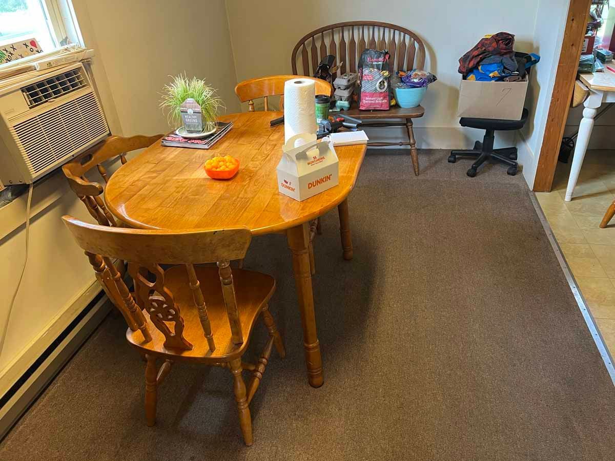 A dining room with a wooden table, chairs, and various items on the table, including tissues and a roll of paper towels.