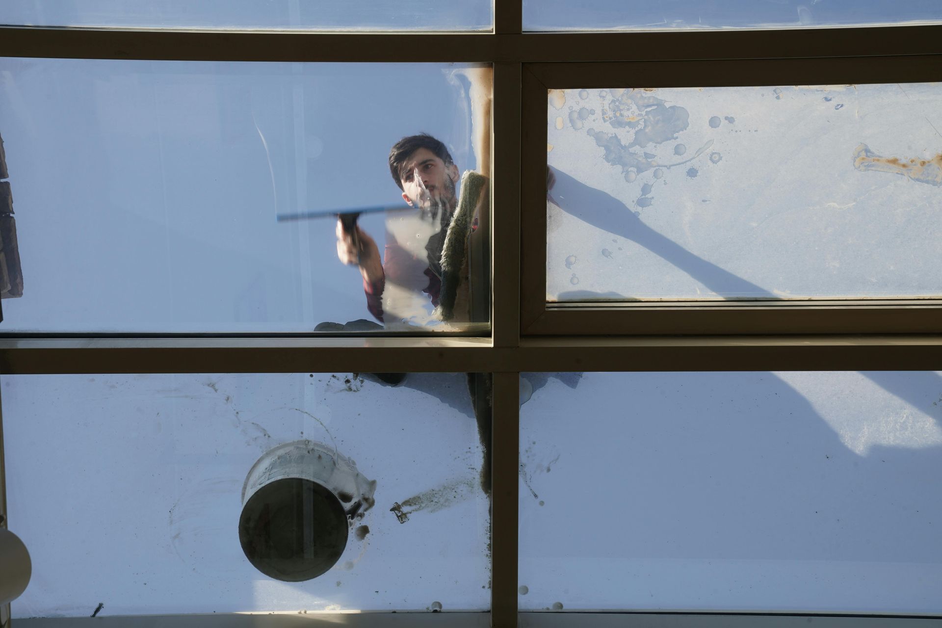 Person using a squeegee to clean a window, seen through the glass; sunny day.