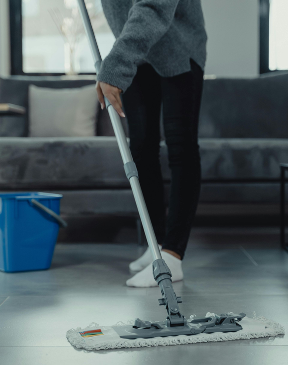 Person mopping a floor. A blue bucket sits nearby.