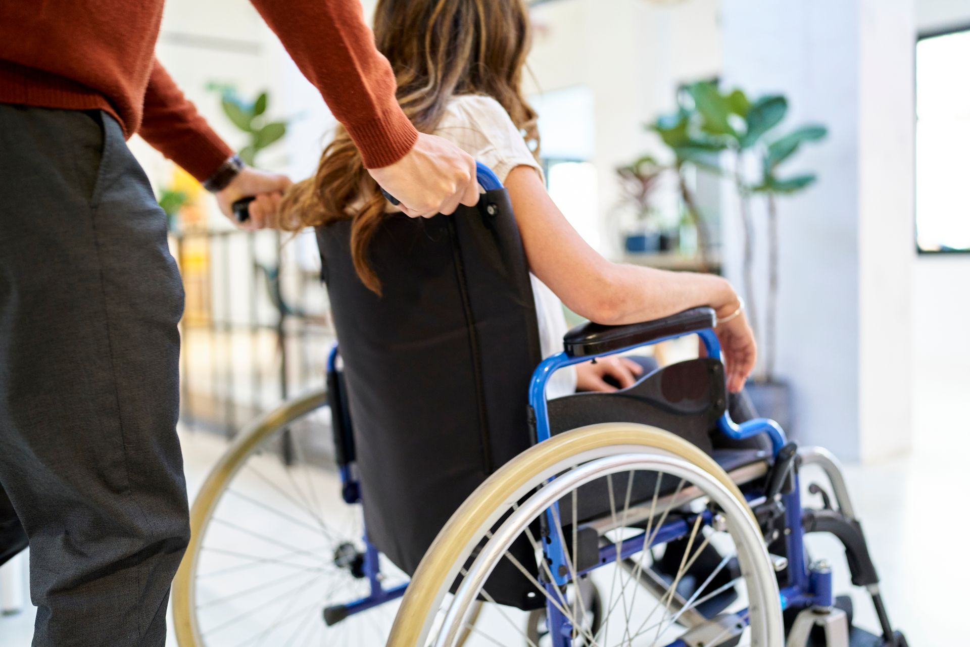 Person pushes a woman in a wheelchair through a modern building.