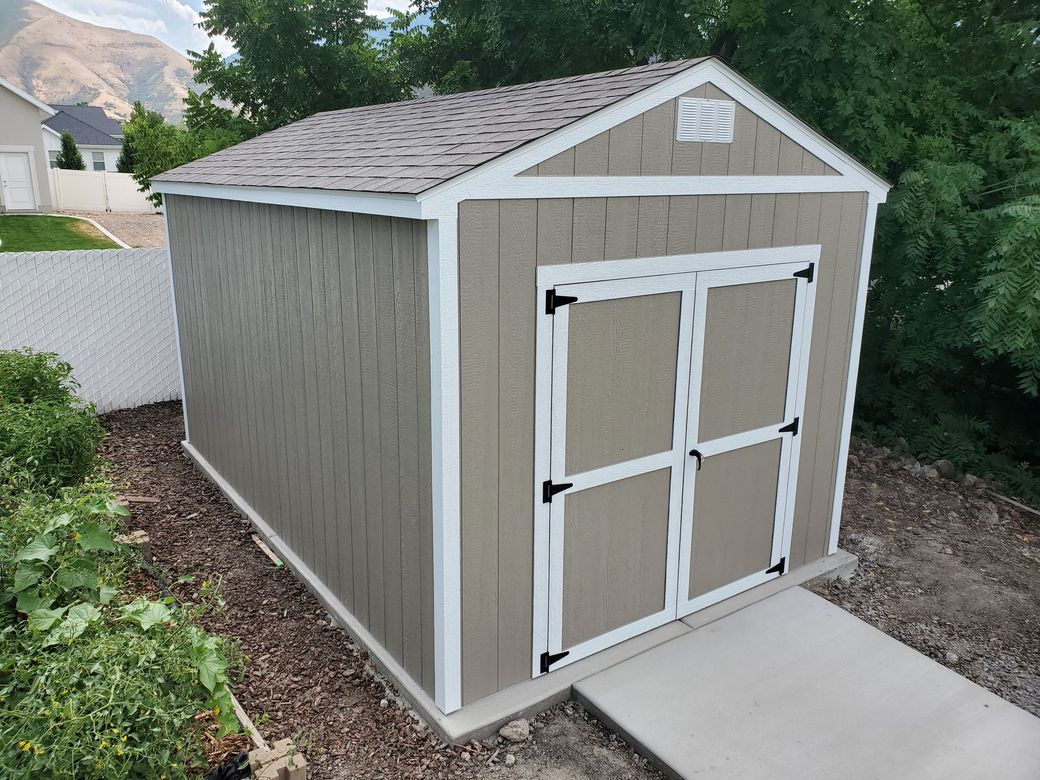 Blue shed with white trim, Dutch barn roof, and windows, set in a yard.