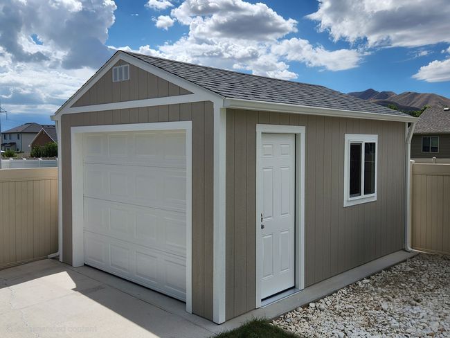 White garage with brown trim, door, and closed garage door on a concrete pad with grass.