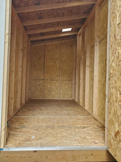 The interior of a wooden shed with unfinished walls and floorboards, showing timber framing and a slanted ceiling.
