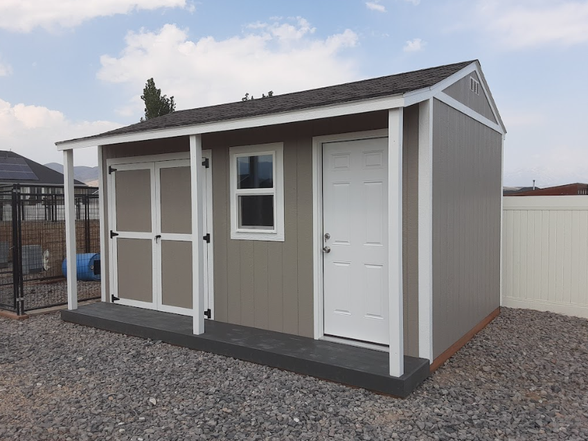 A beige, modern storage shed with a white trim, a single door, a double door, a window, and a small porch on gravel.