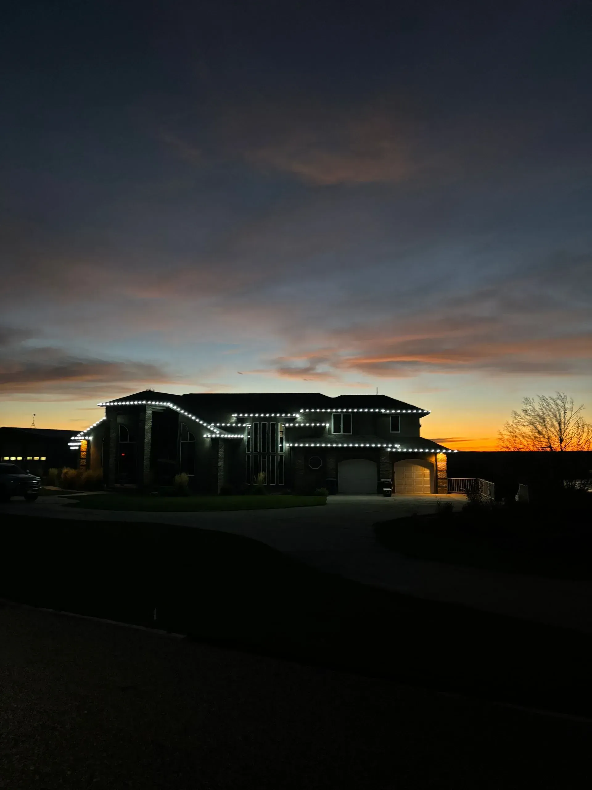 A house is lit up at night with a sunset in the background.