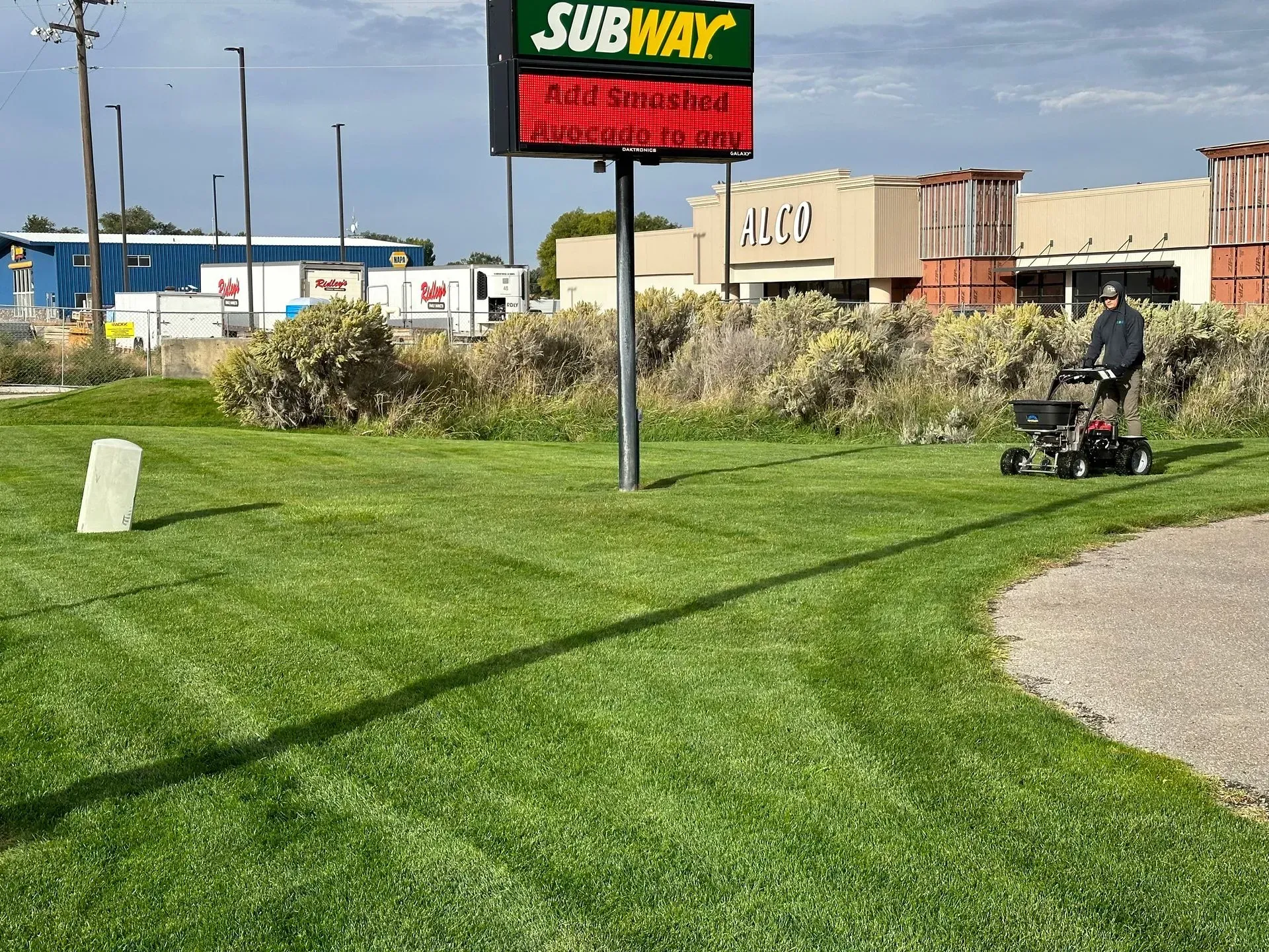 A man is mowing the grass in front of a subway sign.