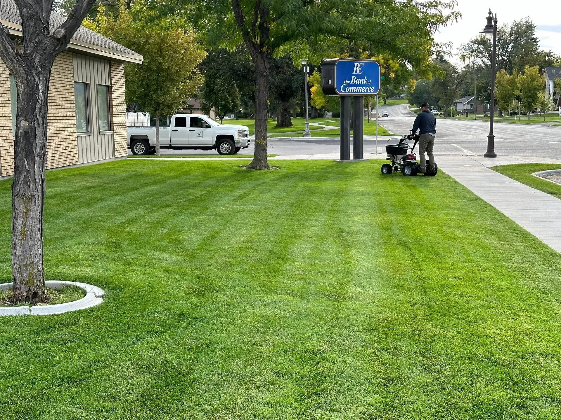 A man is using a lawn mower to cut the grass in front of a building.