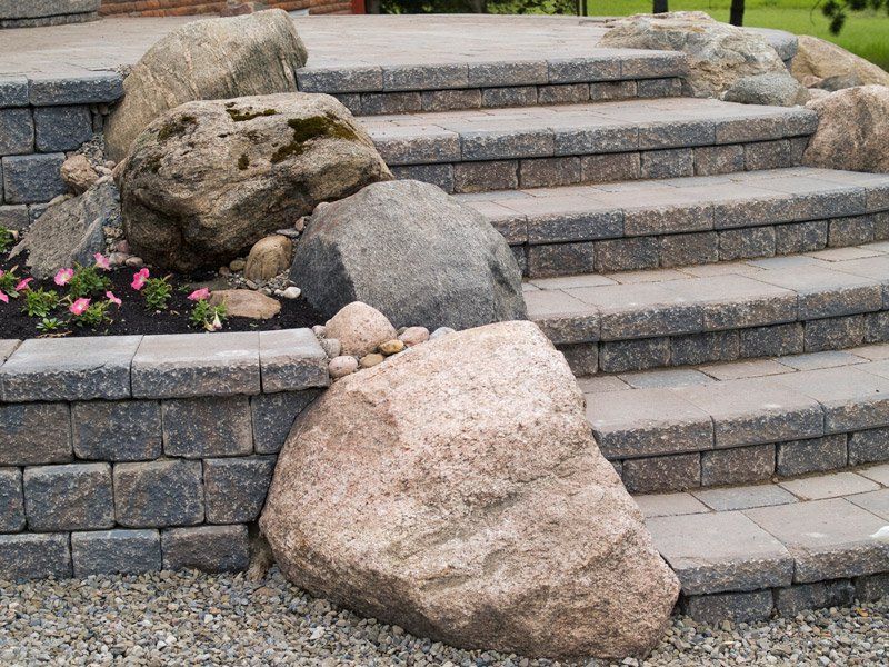 Stone steps and retaining wall with large boulders and small plants.
