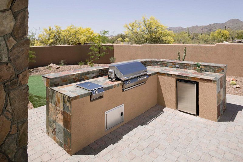 Outdoor kitchen with grill, cooktop, refrigerator, and stone facade, on a brick patio.