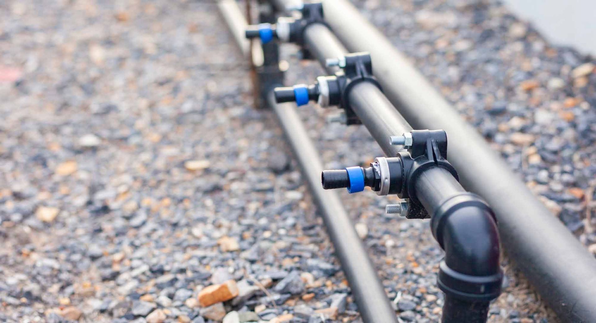 Black pipes with blue connectors in a gravel setting, likely for irrigation or industrial use.