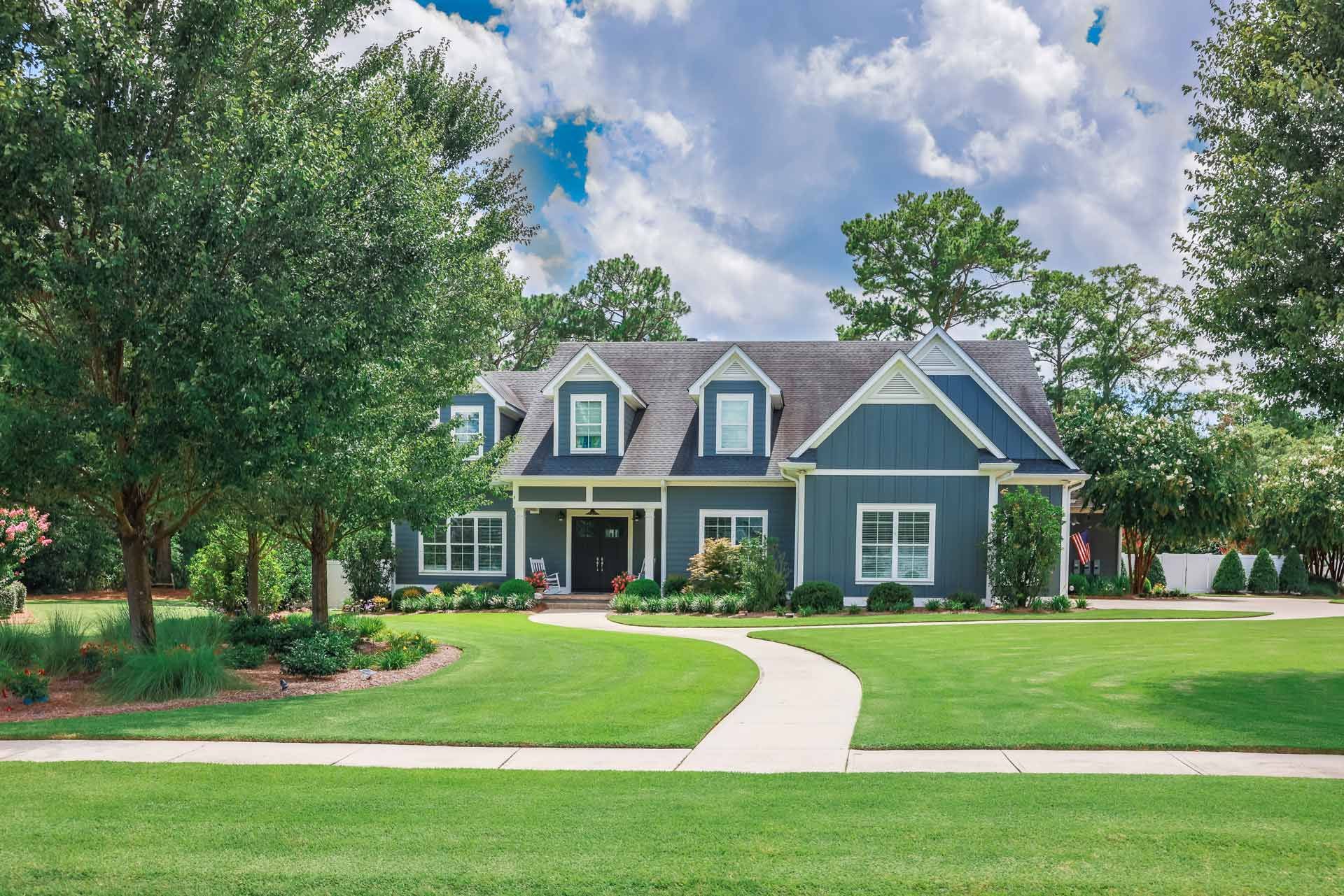 Blue house with white trim, green lawn, and walkway on a sunny day.