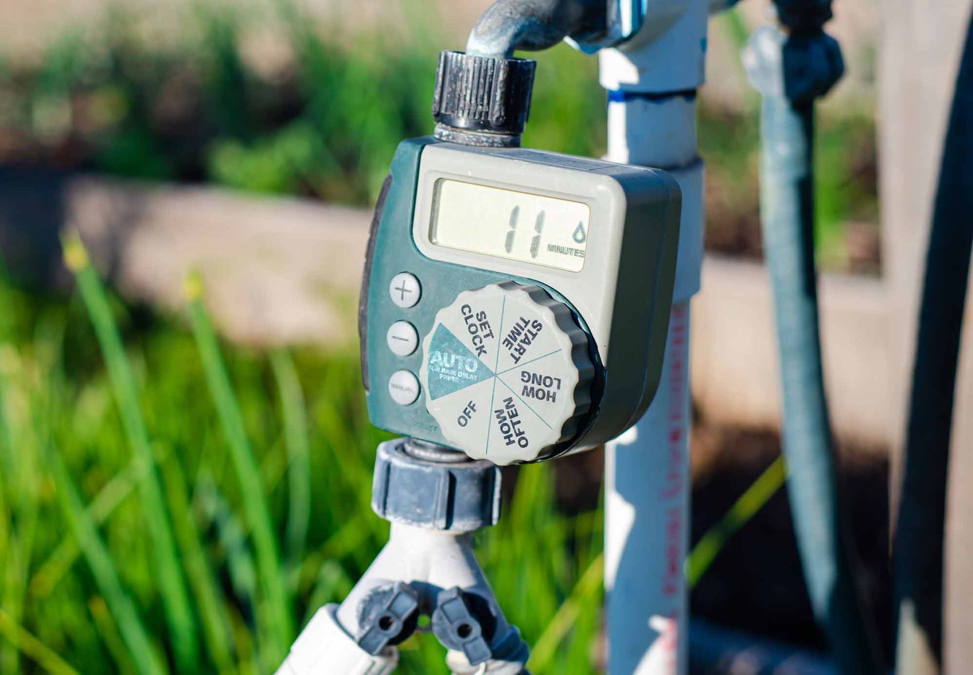 Water timer attached to a faucet, with digital display and control dial, in a garden.