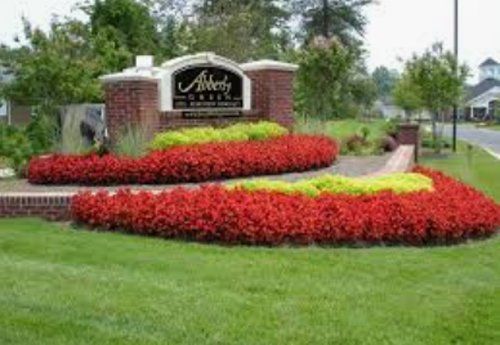 Sign for Alberty Creek subdivision with red and yellow flowers and brick accents.