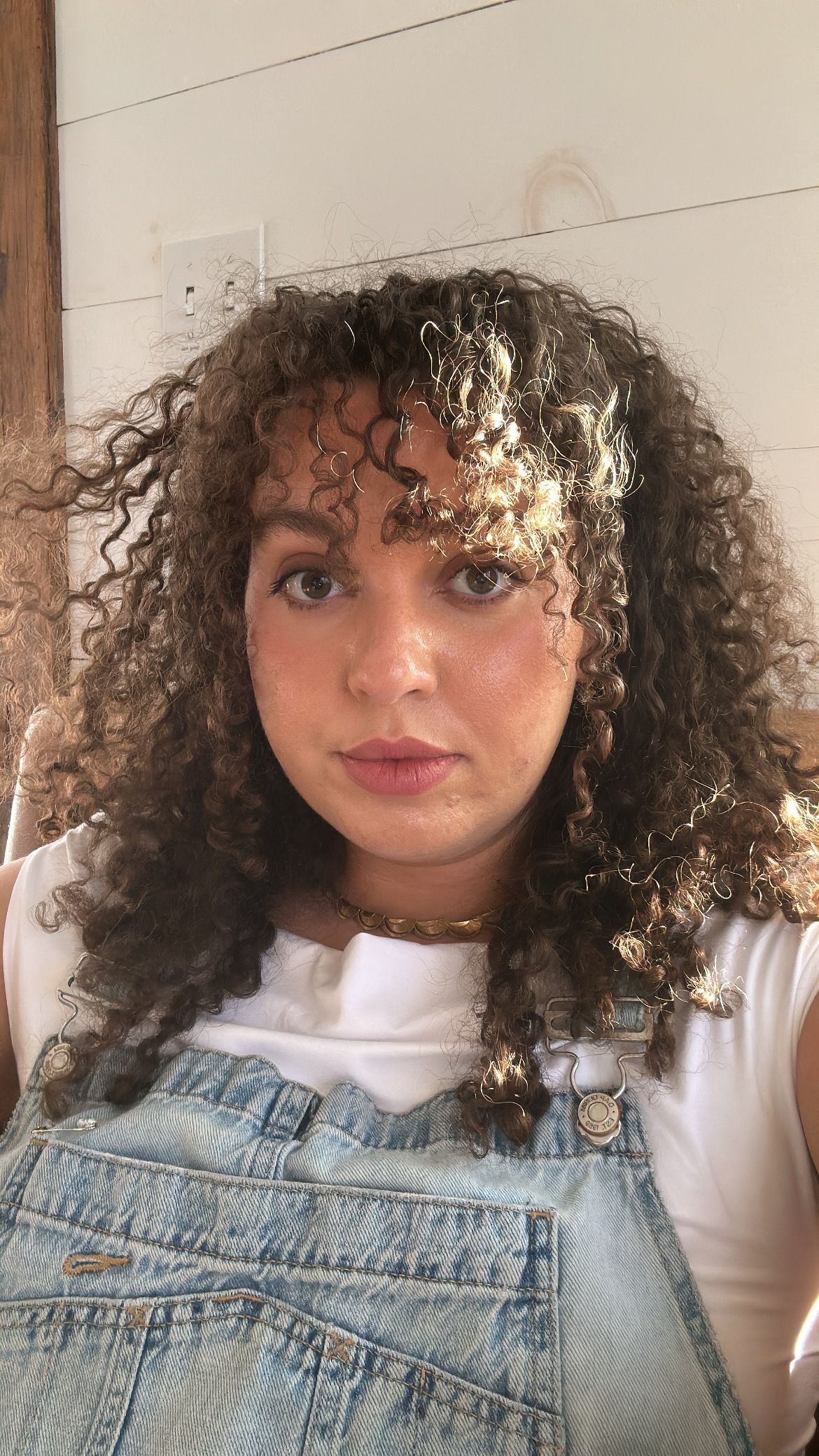 A woman with curly hair is wearing overalls and a white shirt.