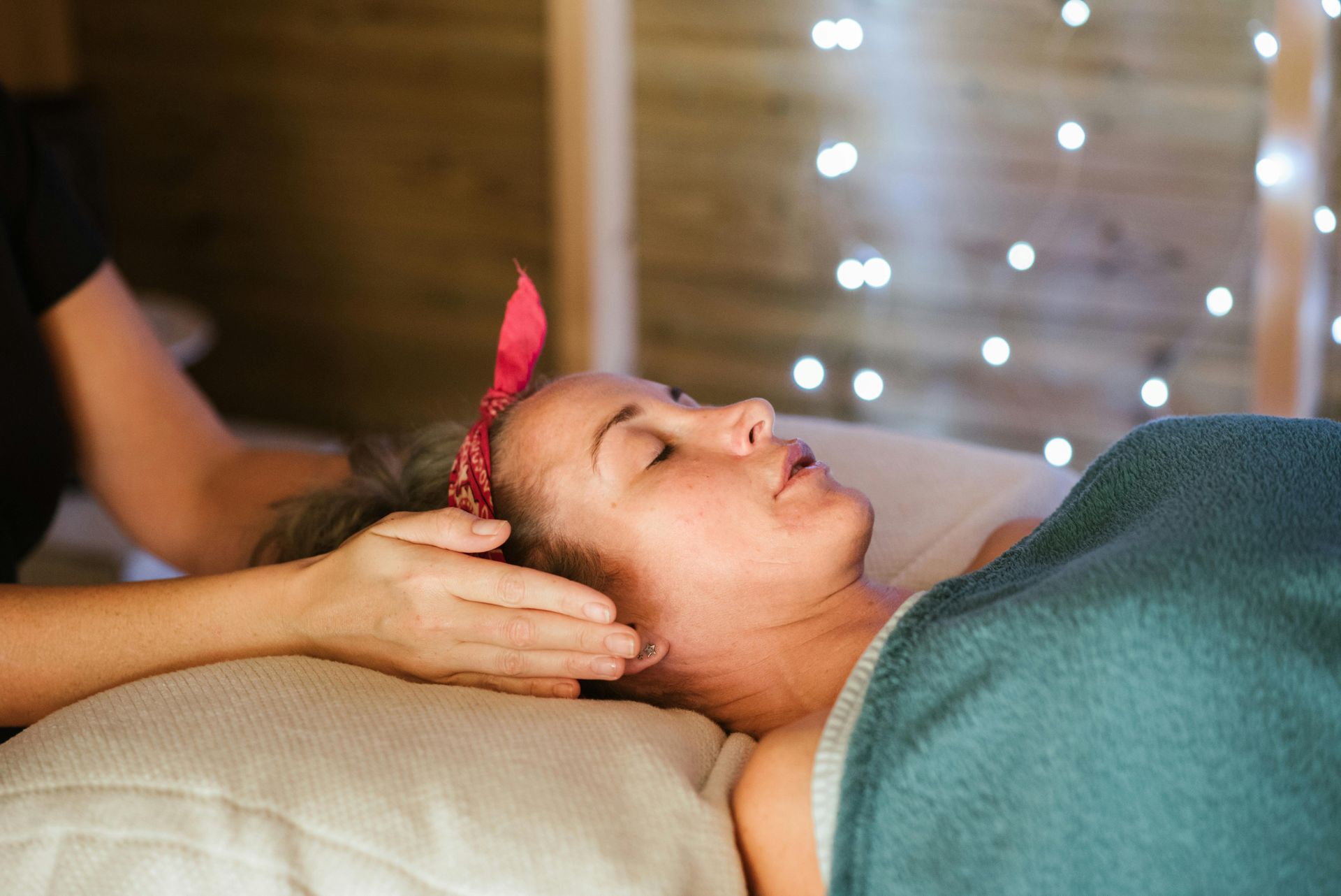 A woman is laying on a bed getting a head massage.