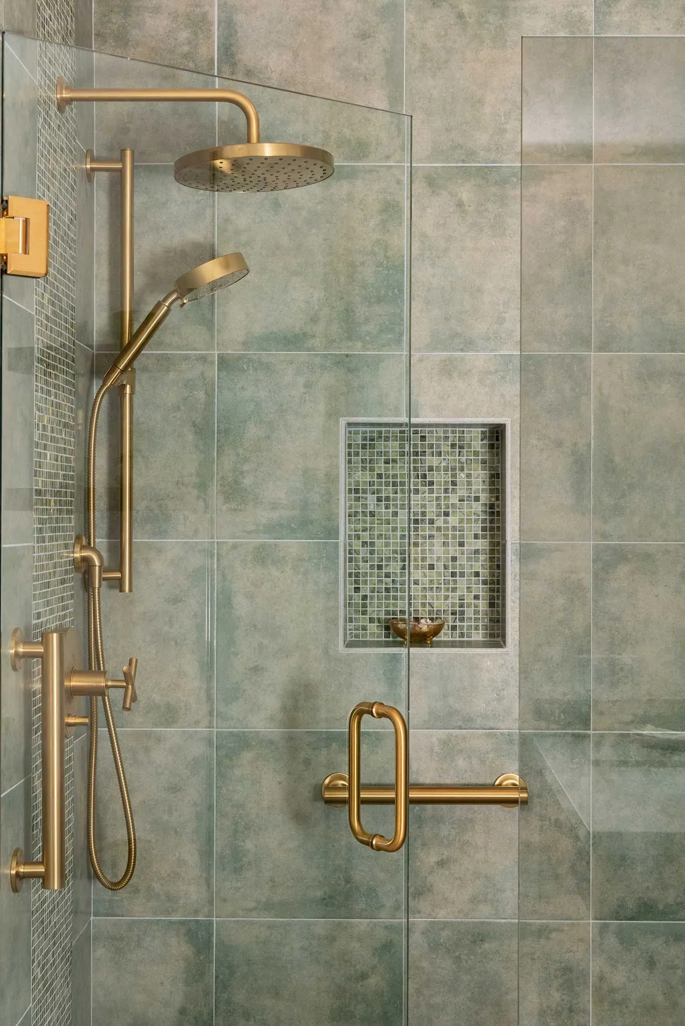 A shower with a glass door and a brass shower head.