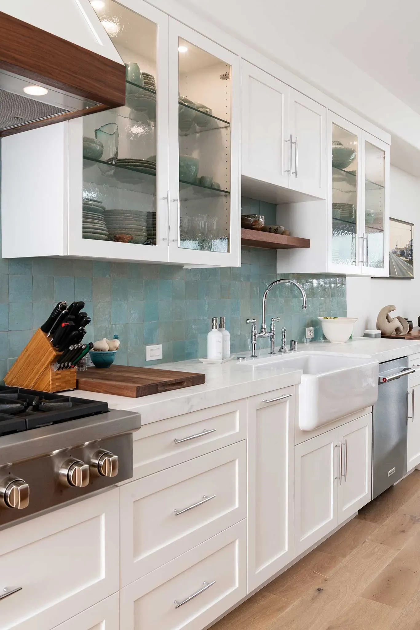 A kitchen with white cabinets , a stove , a sink , and a cutting board.
