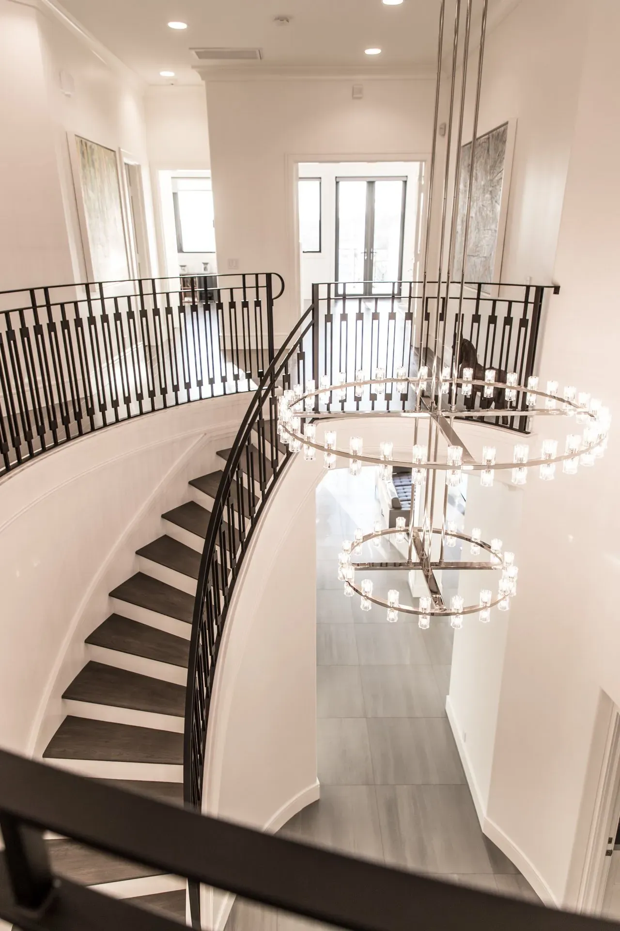 A spiral staircase with a wrought iron railing and a chandelier hanging from the ceiling.