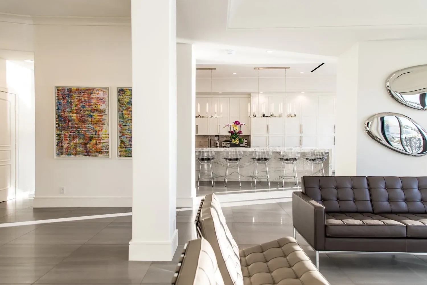 A living room with a couch and two chairs and a kitchen in the background.