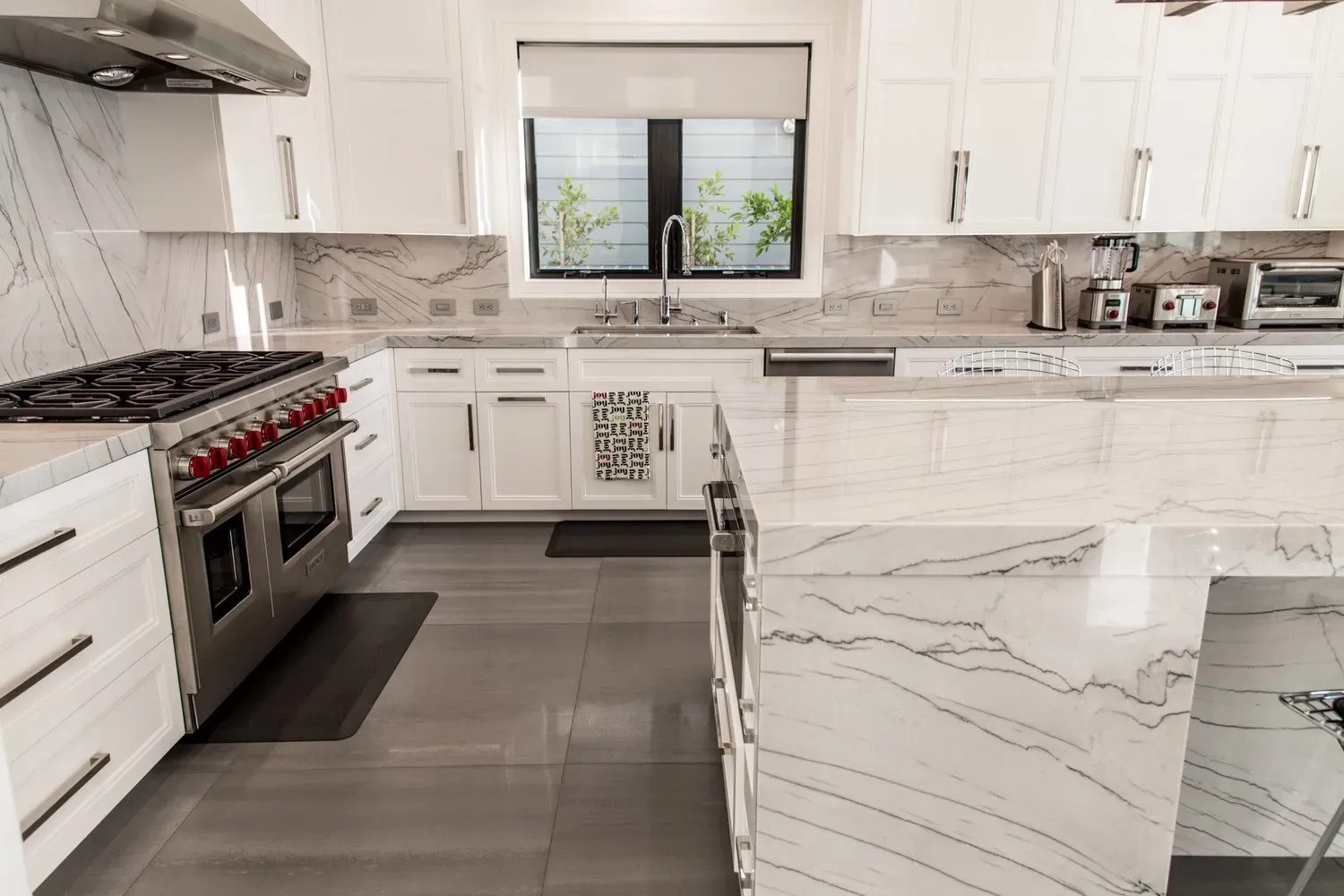 A kitchen with white cabinets , stainless steel appliances , marble counter tops and a large island.